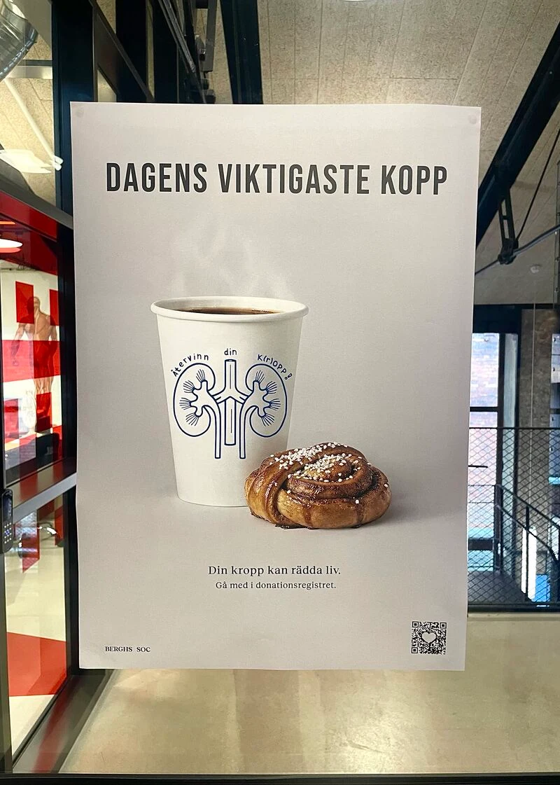 Dagens viktigaste kopp poster installed at Berghs, featuring the kidney cup, a cinnamon bun and a donation-register QR code.
